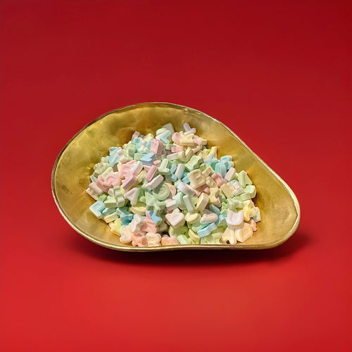 Multiple coloured letter shaped chalky textured alphabet letters in a gold bowl with a red background 