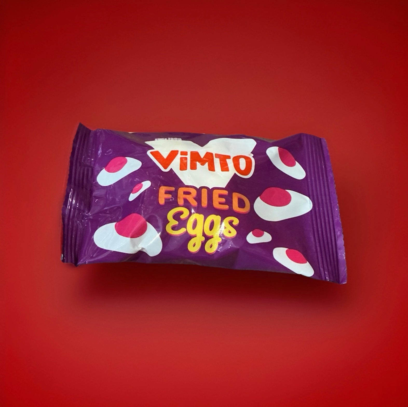 Vimto flavoured jelly sweets in the shape of fried eggs in a purple wrapper on a red background 