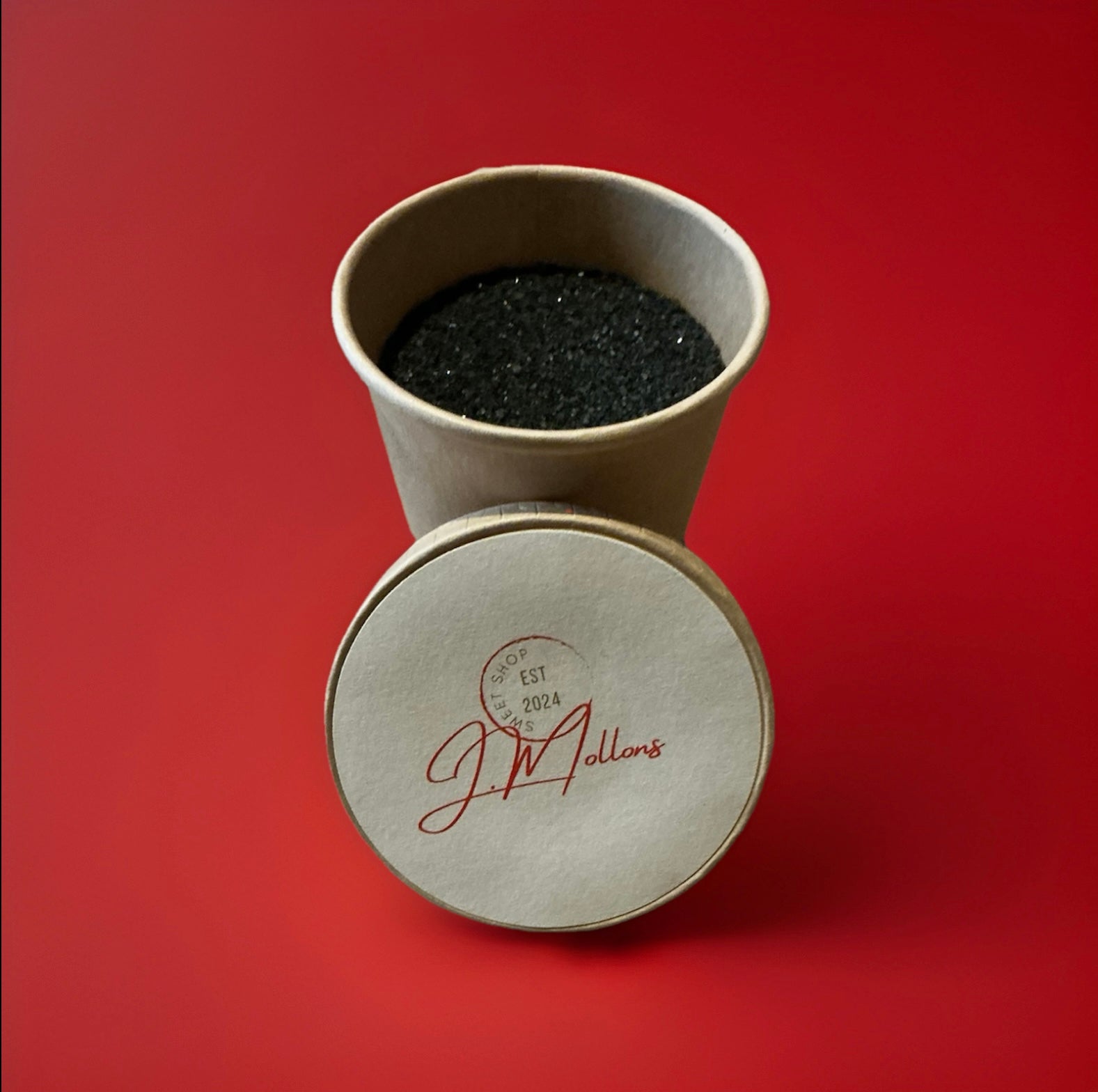 Black coal dust liquorice flavoured sherbet in a brown paper pot on a red background 
