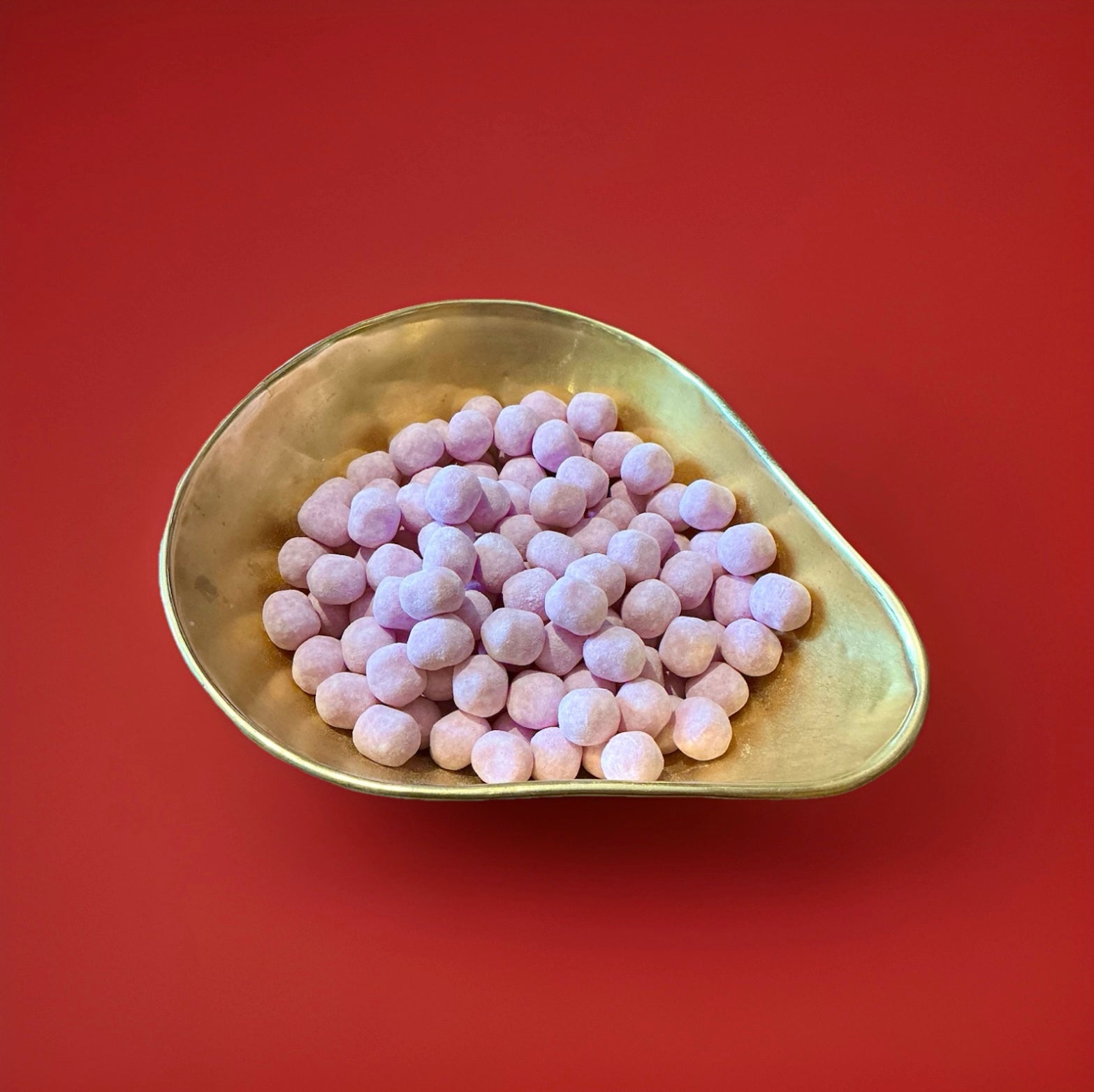 Round shaped purple coloured Vimto flavoured Bon Bon’s in a gold bowl on a red background 
