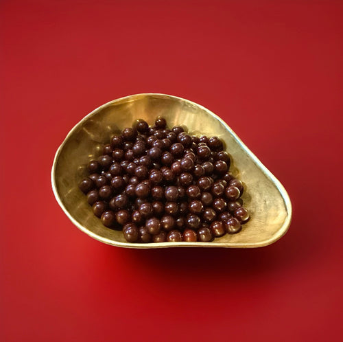 Red coloured aniseed balls in a gold bowl on a red background 