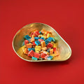 Multicoloured fruit flavoured jelly sweets in the shape of a brick with a white fondant centre and a fizzy sugar coating in a gold bowl with a red background 