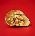 Square pieces of clotted cream fudge in a gold bowl with a red background 