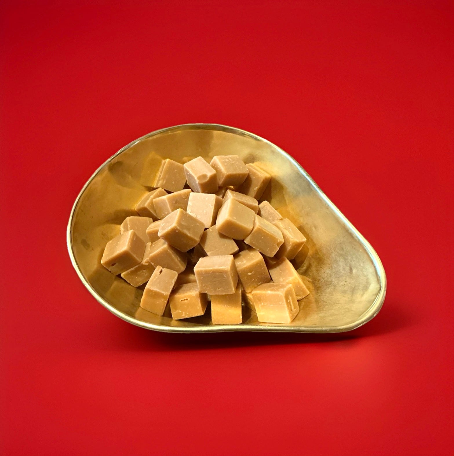 Square pieces of clotted cream fudge in a gold bowl with a red background 