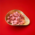 Pink strawberry flavoured chocolate in the shape of pigs in a gold bowl on a red background 
