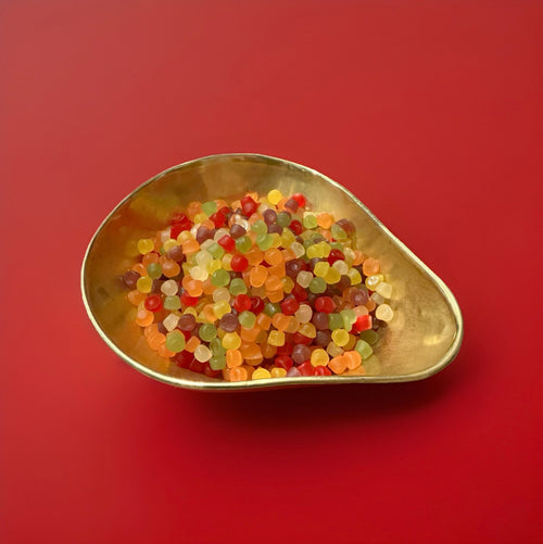 Small round floral flavoured gummy sweets in a gold bowl with a red background 