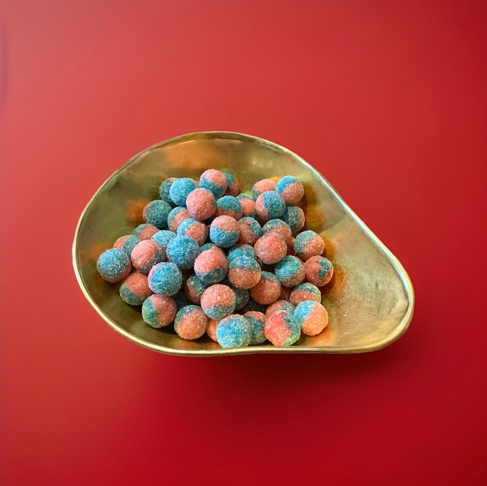 Hard boiled round shaped pink and blue sweet covered in malic acid in a gold bowl on a red background 