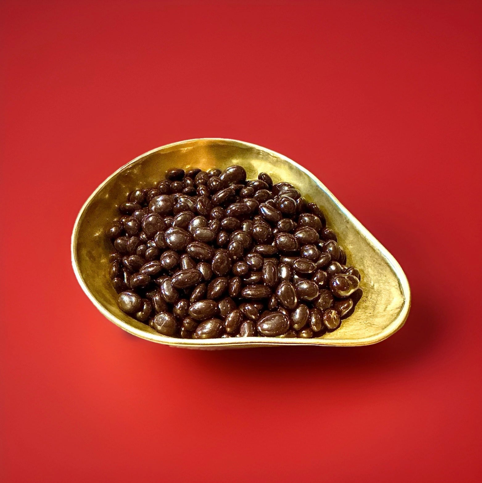 Raisins coated in dark chocolate in A gold bowl on a red background 