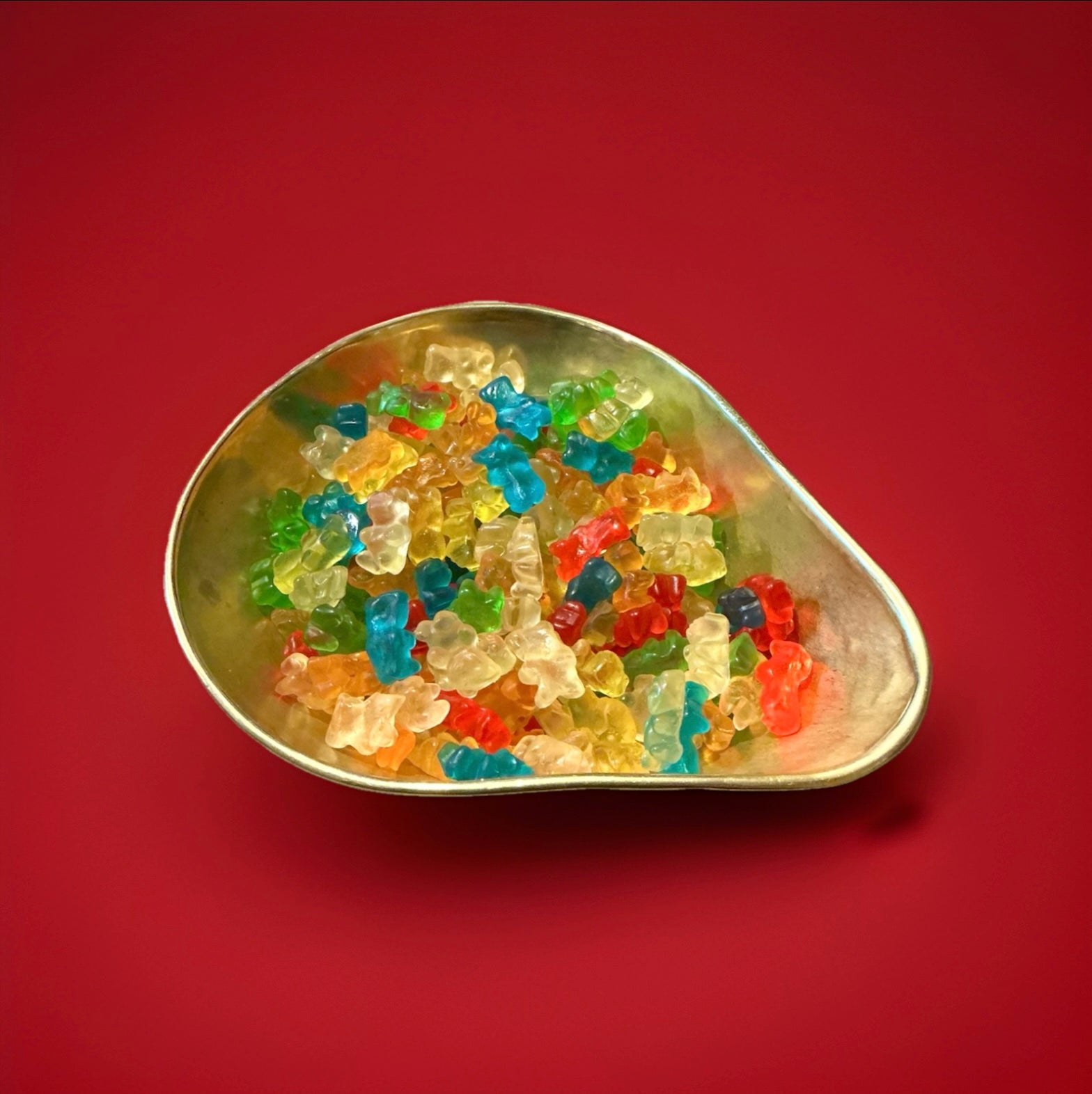 Teddy bear shaped fruit flavoured jelly sweets in a gold bowl on a red background 