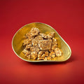 Clusters of peanut brittle in a gold bowl on a red background 