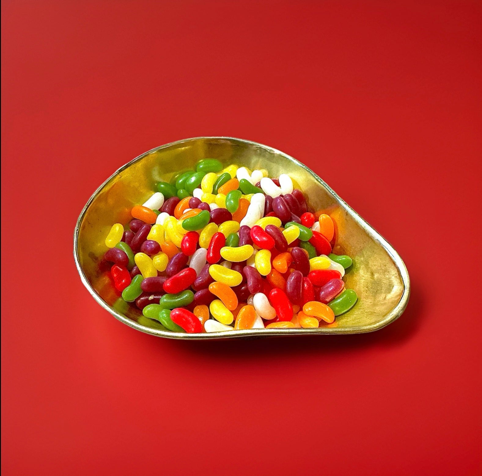 Multicoloured fruit flavoured Barratt jelly beans in a gold bowl on a red background 