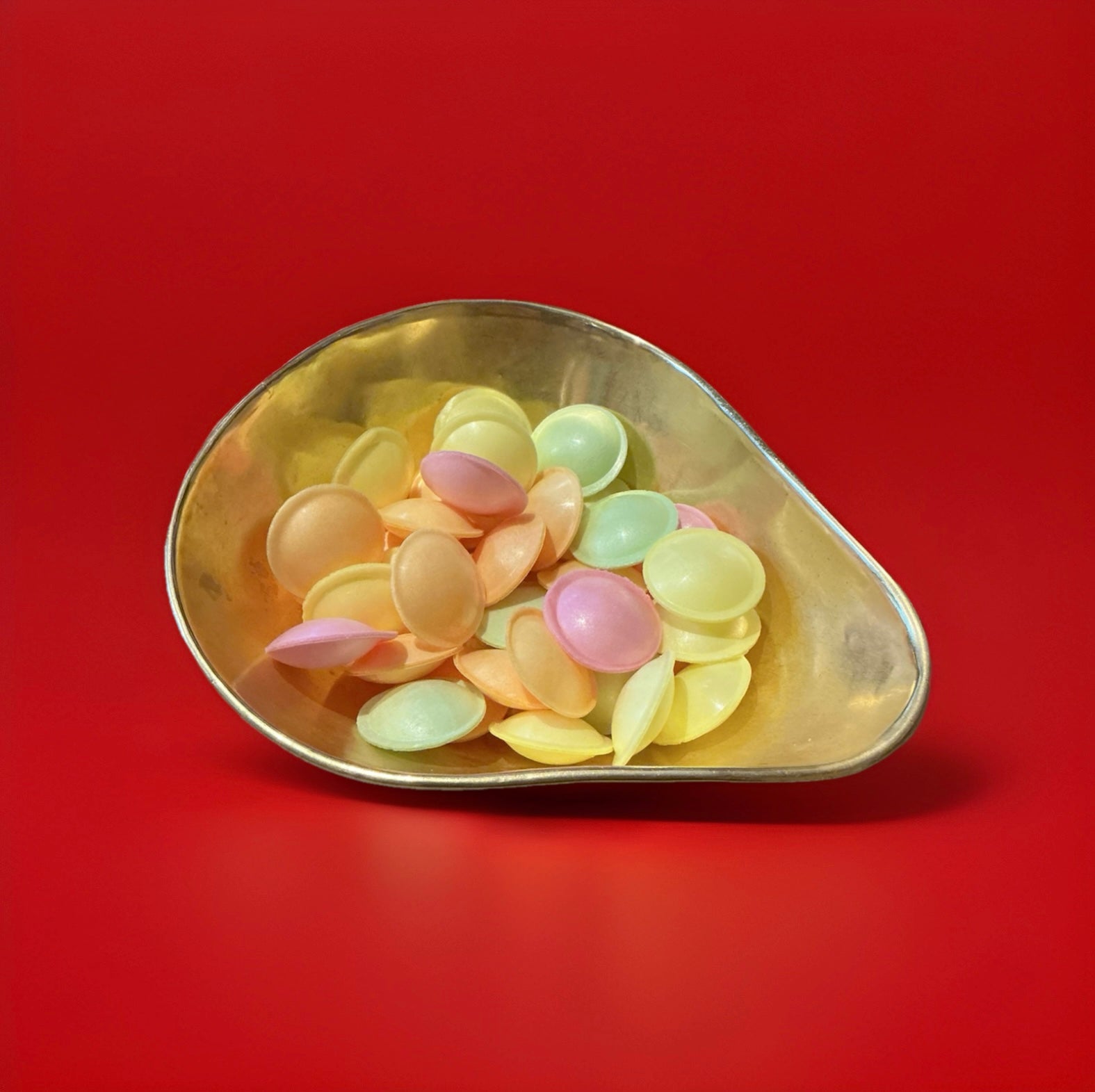 A plastic cone of flying saucers made of rice paper and sherbet in a gold bowl with a red background 
