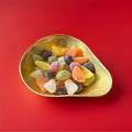 Multicoloured large fruit shaped fruit jellies in a gold bowl on a red background 