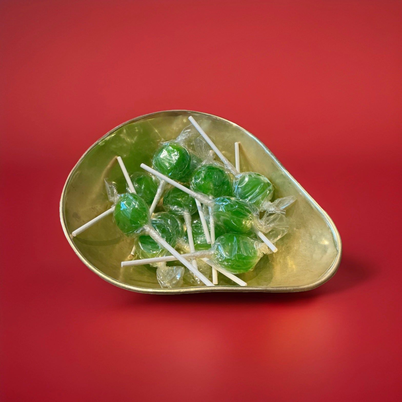Individually wrapped green apple flavoured lolly in a gold bowl on a red background 