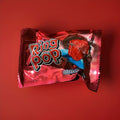 A hard boiled diamond shaped lolly mounted on a plastic ring in a foil wrapper on a red background 