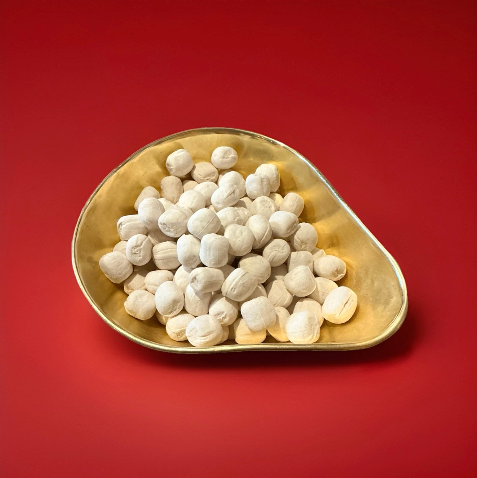 Ginger coloured ginger flavoured oval shaped soft rock sweets in a gold bowl on a red background 