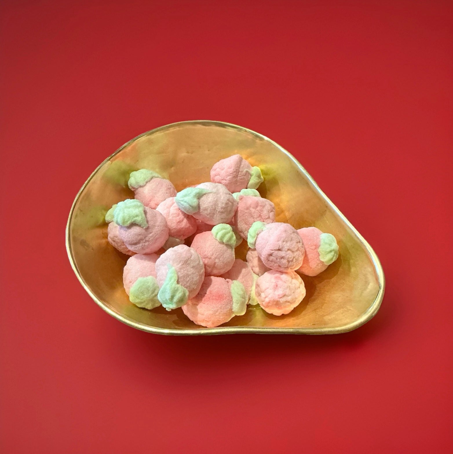 Large raspberry shaped marshmallow with a jelly centre green and pink in colour in a gold bowl with a red background 