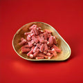 Red liquorice tubes with a white fondant centre coated in fizzy sugar in a gold bowl with a red background 