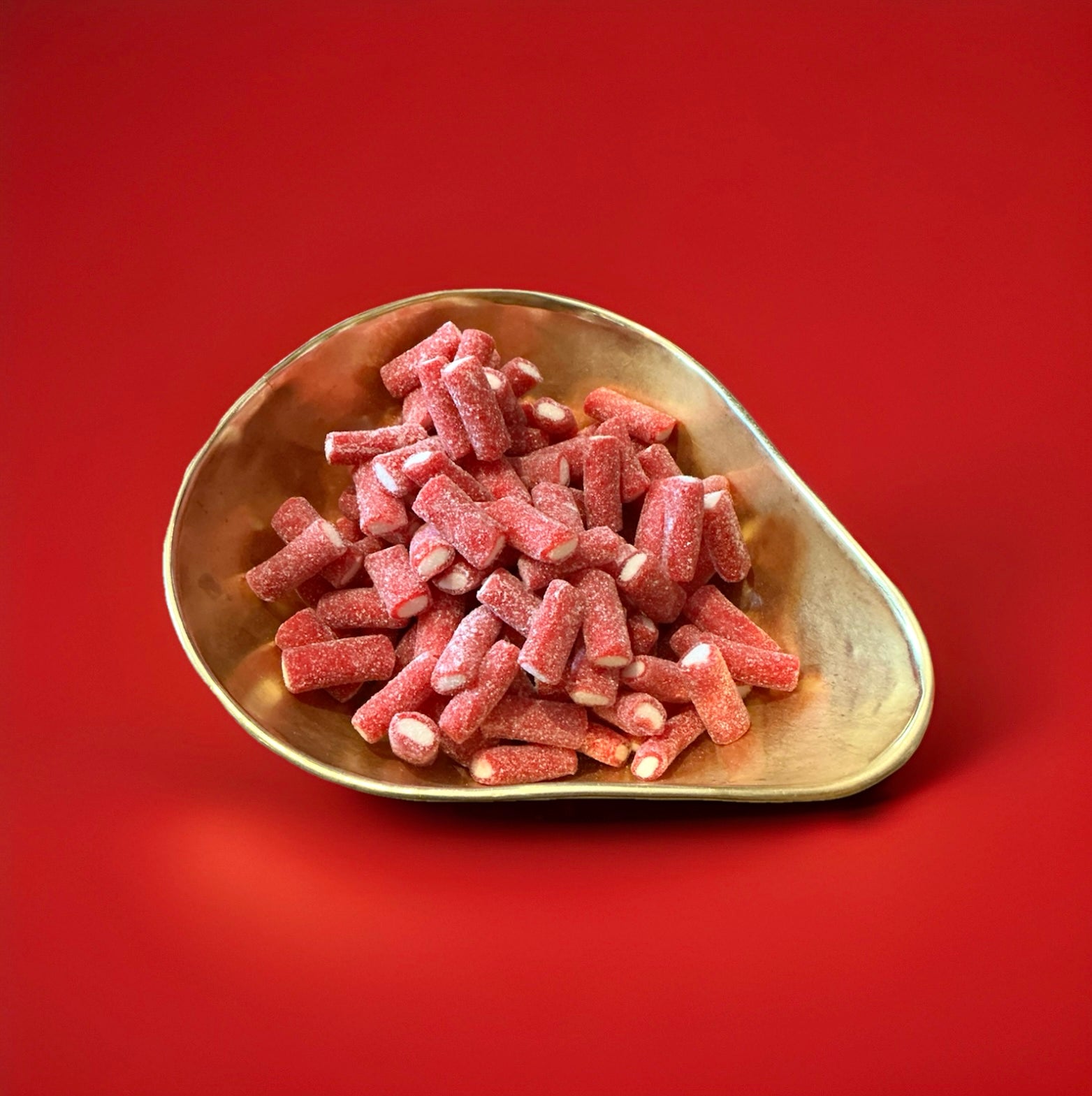 Red liquorice tubes with a white fondant centre coated in fizzy sugar in a gold bowl with a red background 