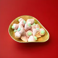 Large light pink and green coloured strawberry flavoured marshmallows with a jelly centre in a gold bowl with a red background 