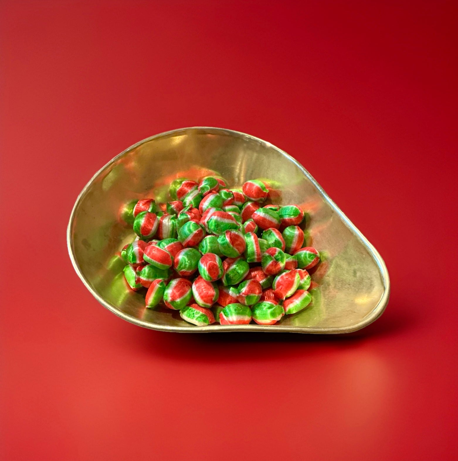 Red white and green round hard boiled sweets with an apple flavour and a fizzy sherbet centre in a gold bowl with a red background 