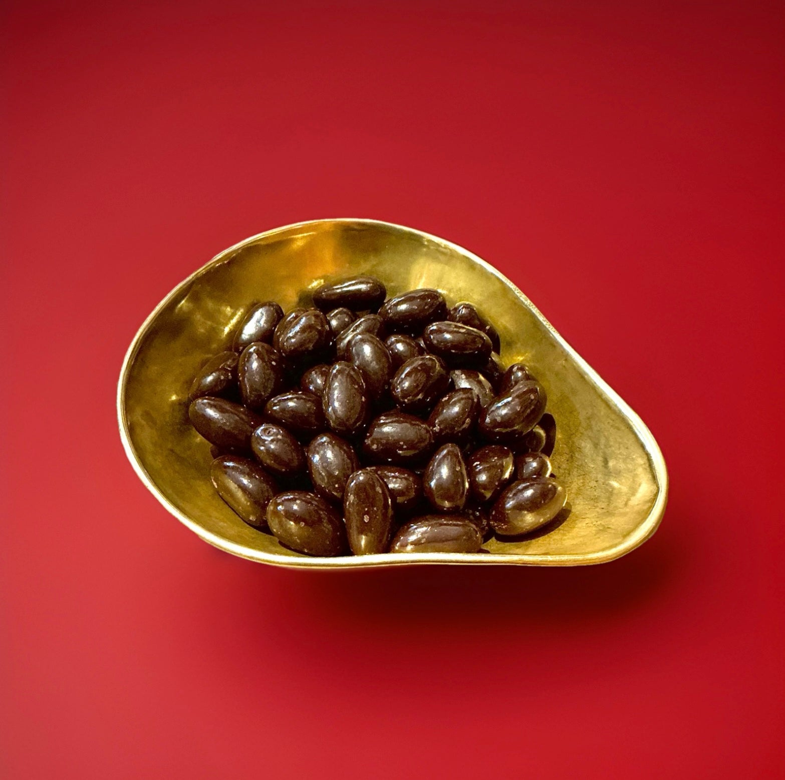 Dark chocolate coated Brazil nuts in a gold bowl on a red background 