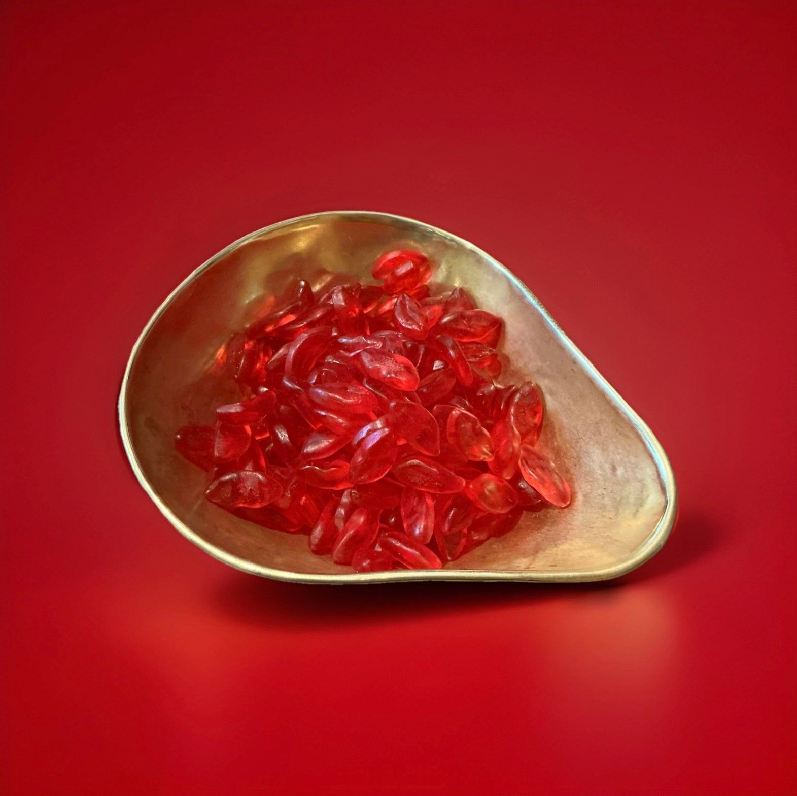 Fruity lip shaped red jelly sweets in a gold bowl on a red background 