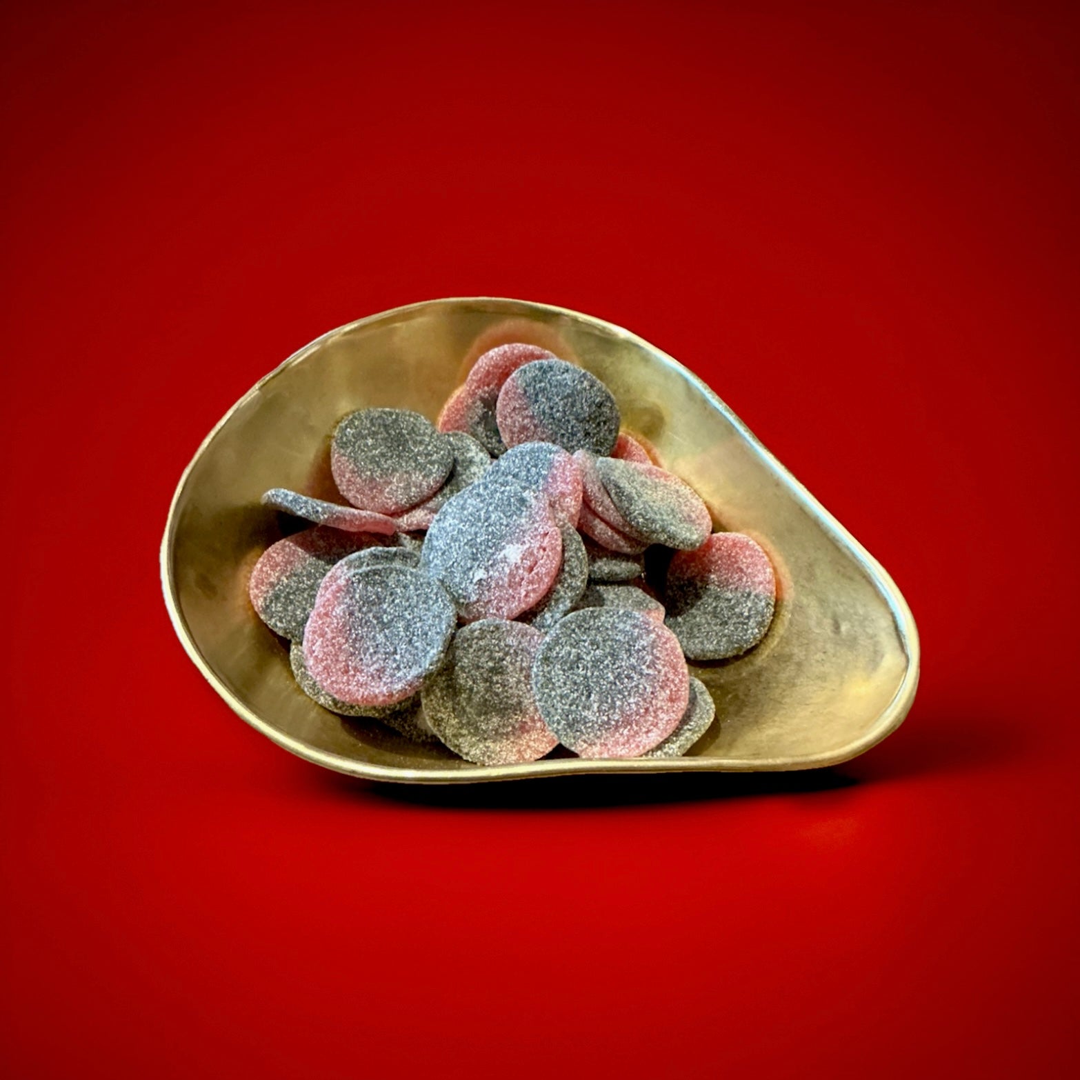 Large disc shaped fizzy raspberry and liquorice sunsets in a gold bowl with a red background 