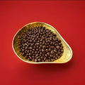 Roasted coffee beans coated in dark chocolate in a gold bowl on a red background 