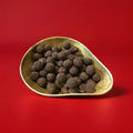 Round ball shaped rum truffles with chocolate sprinkles in a gold bowl on a red background 