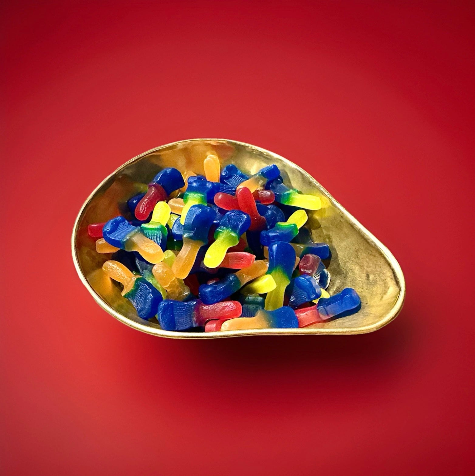 Multicoloured paintbrush shaped tongue painter jelly sweets in a gold bowl on a red background 