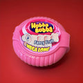 Fruit flavoured bubblegum tape in a pink plastic container on a red background 
