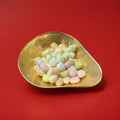 Multicoloured fruit flavoured oval shaped soft rock sweets in a gold bowl on a red background 