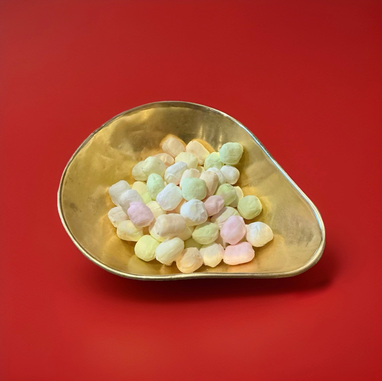 Multicoloured fruit flavoured oval shaped soft rock sweets in a gold bowl on a red background 