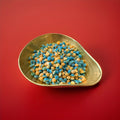 Orange white and blue colour small round hard boiled pips with an iron brew flavour in a gold bowl with a red background 
