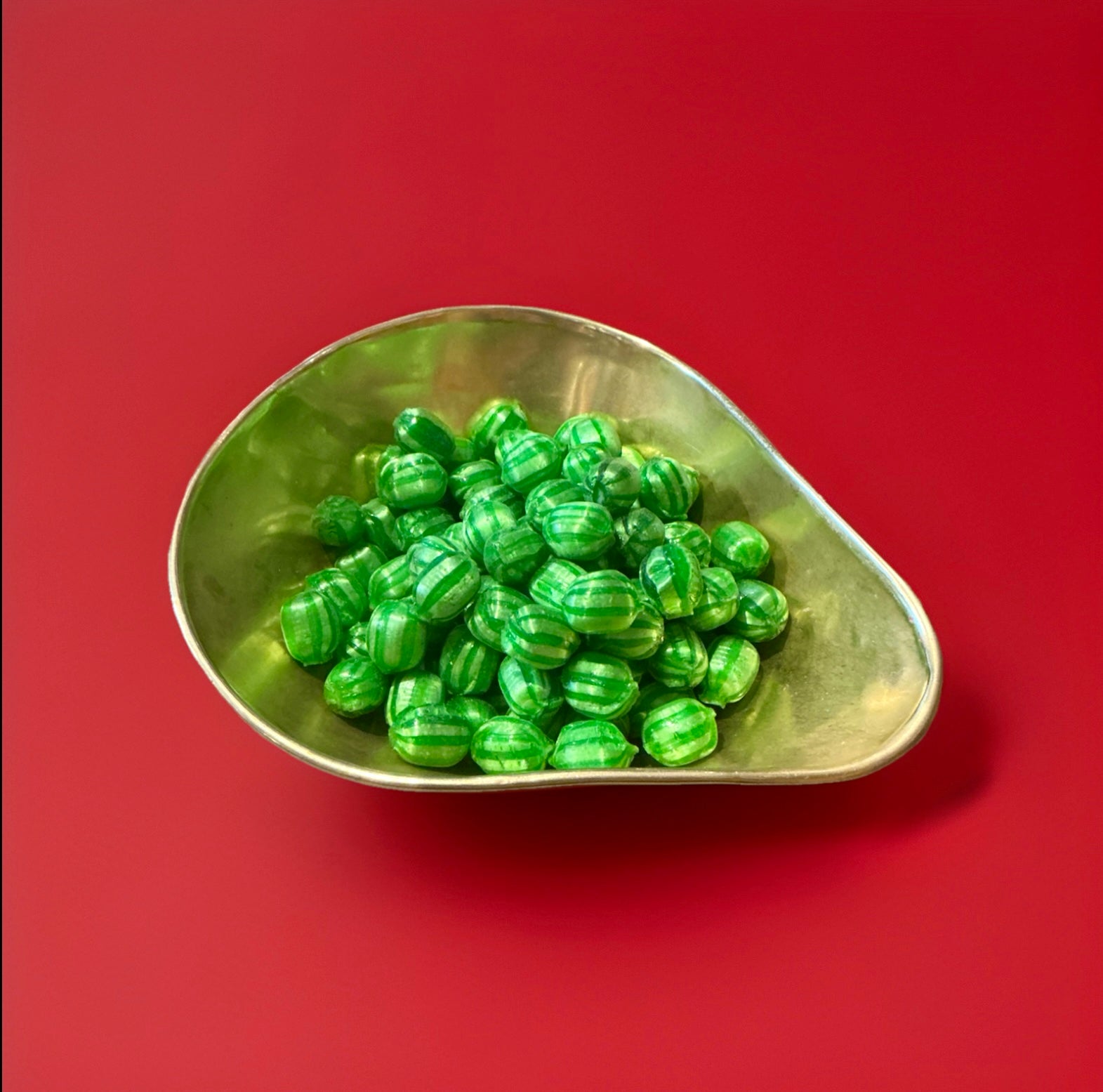 Dark and light green striped hard boiled round sweets with a watermelon flavour and a fizzy sherbet centre in a gold bowl with a red background 