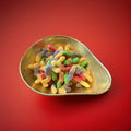 Multicoloured worm shaped jelly sweets with a fizzy sugar coating in a gold bowl with a red background 