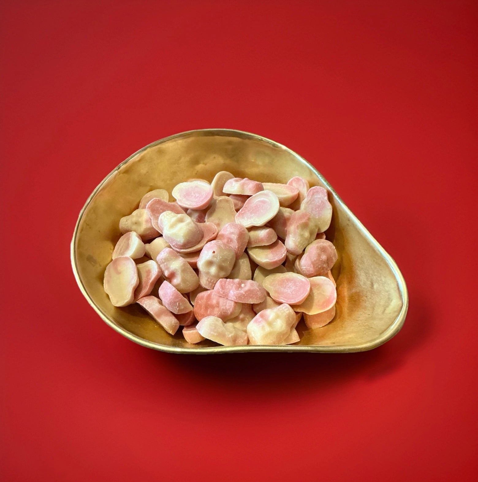 White and strawberry flavoured chocolate in the shape of skulls in a gold bowl on a red background 