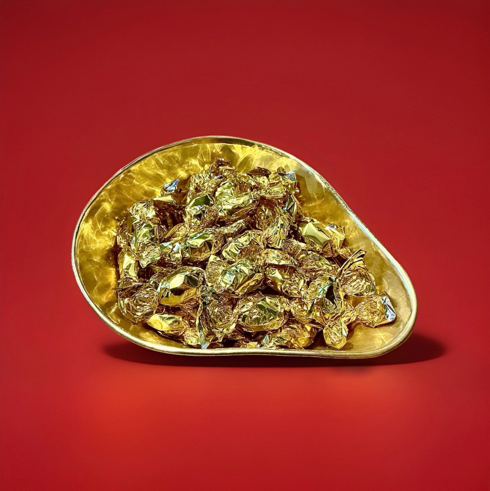 Individually wrapped hard boiled butterscotch sweets in gold wrappers in a gold bowl with a red background 