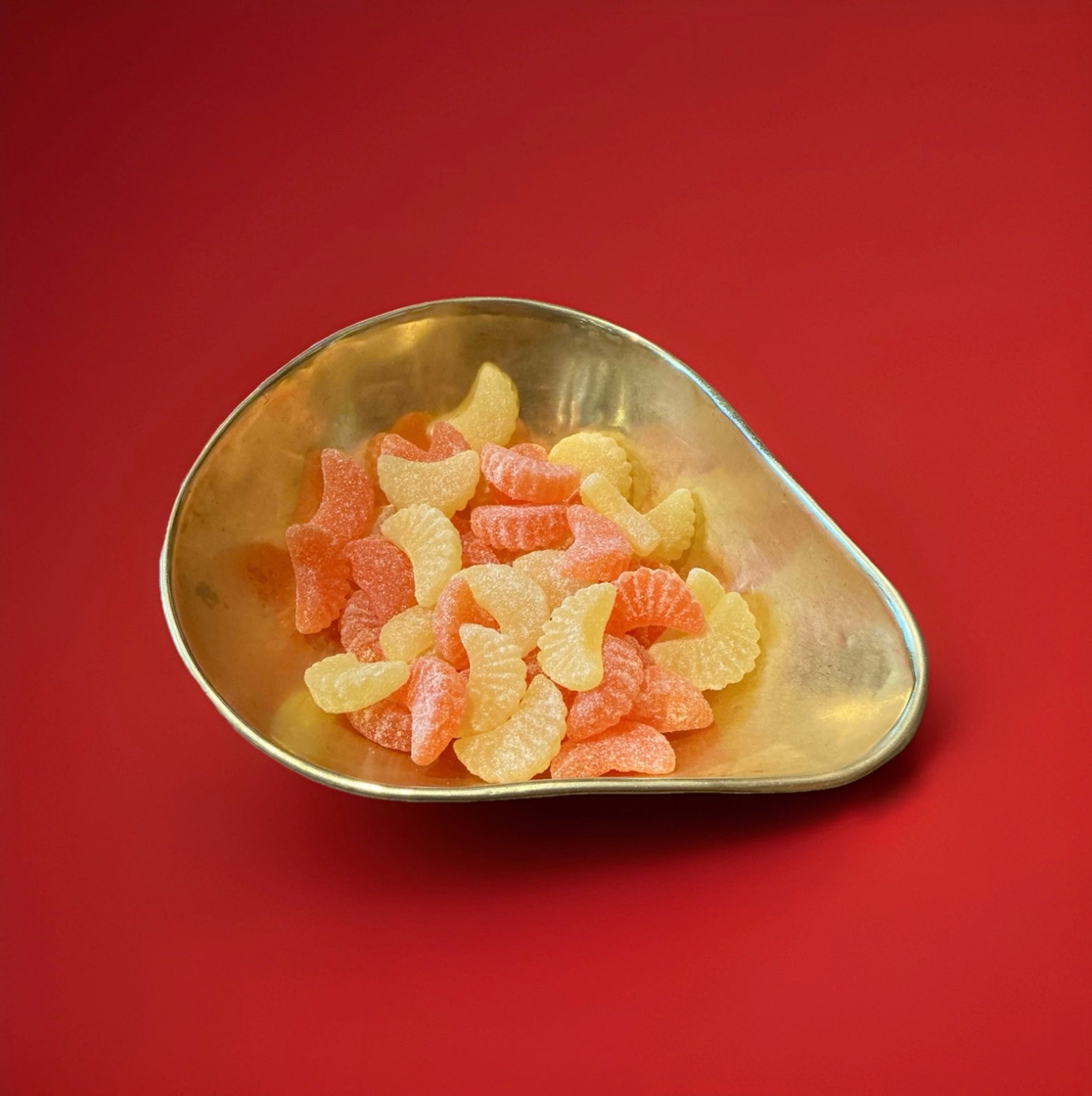 Orange and lemon segment shaped jelly sweets with orange and lemon flavour and a sour sugar coating in a gold bowl with a red background 