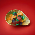 Multicoloured disc shaped smiley face gummy jelly sweets in a gold bowl on a red background 