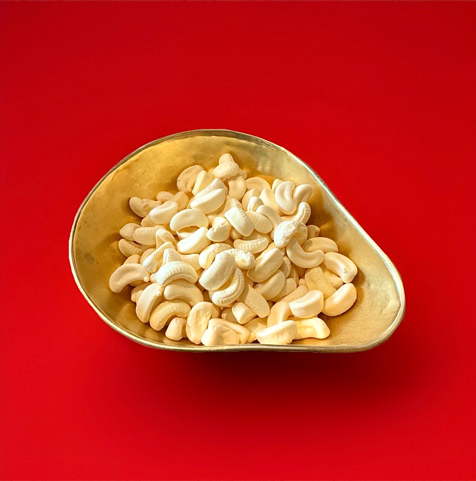 Banana shaped yellow mini foam bananas in a gold bowl with a red background 