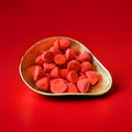 Large bright red marshmallows coated in sugar in a gold bowl with a red background 