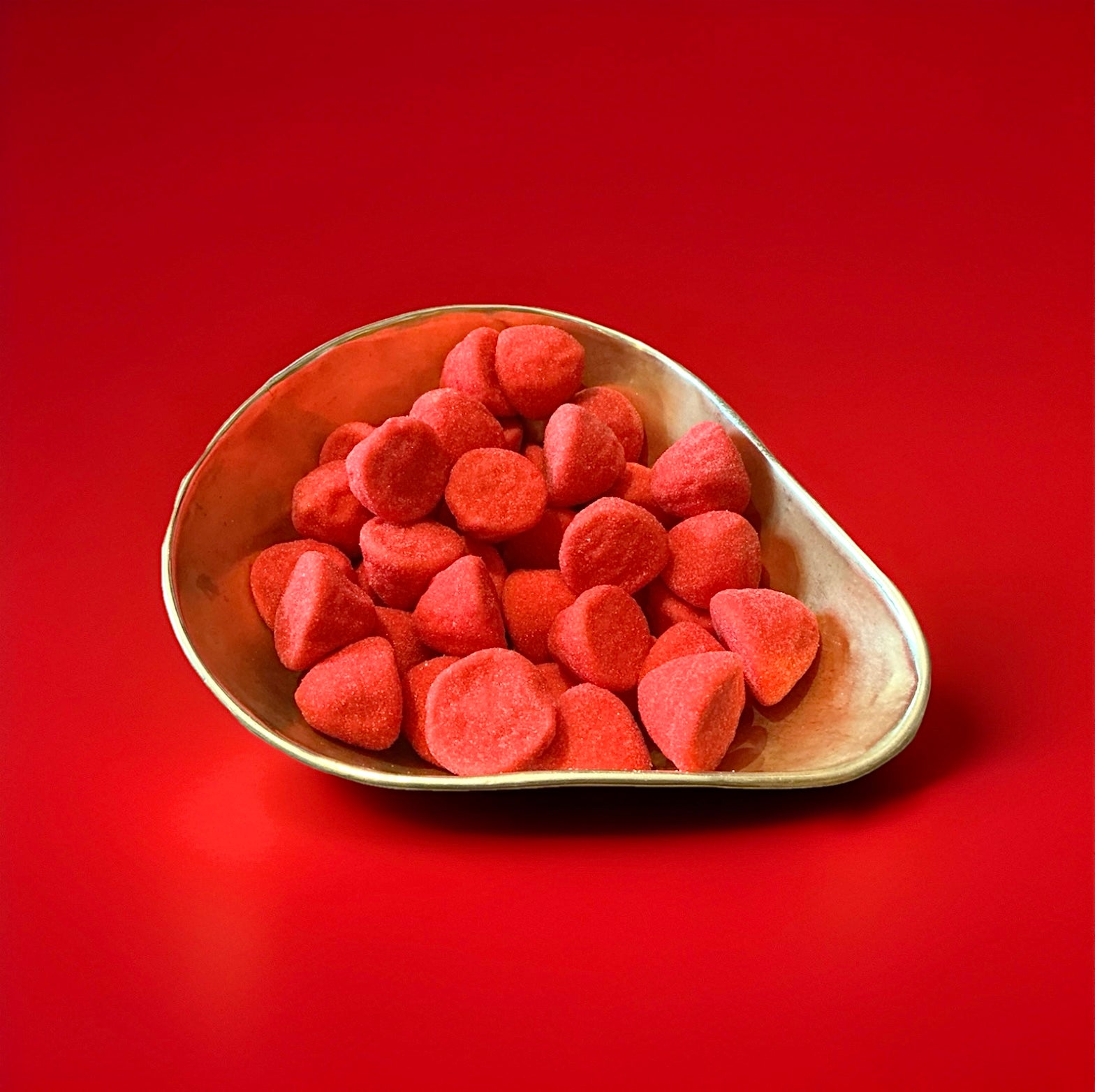 Large bright red marshmallows coated in sugar in a gold bowl with a red background 