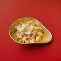 Bite sized pieces of candied stem ginger in a gold bowl with a red background 
