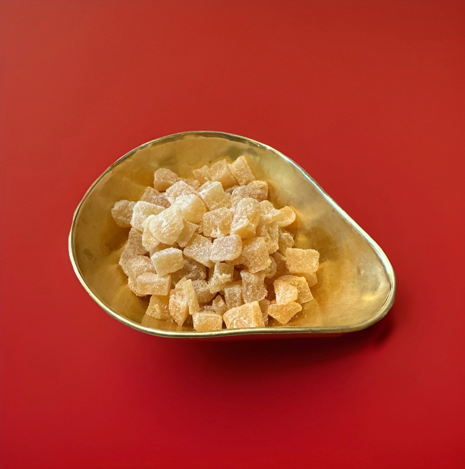 Bite sized pieces of candied stem ginger in a gold bowl with a red background 