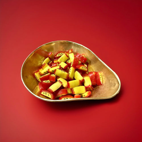 Red and yellow passion fruit flavoured sweets in a gold bowl with a red background 