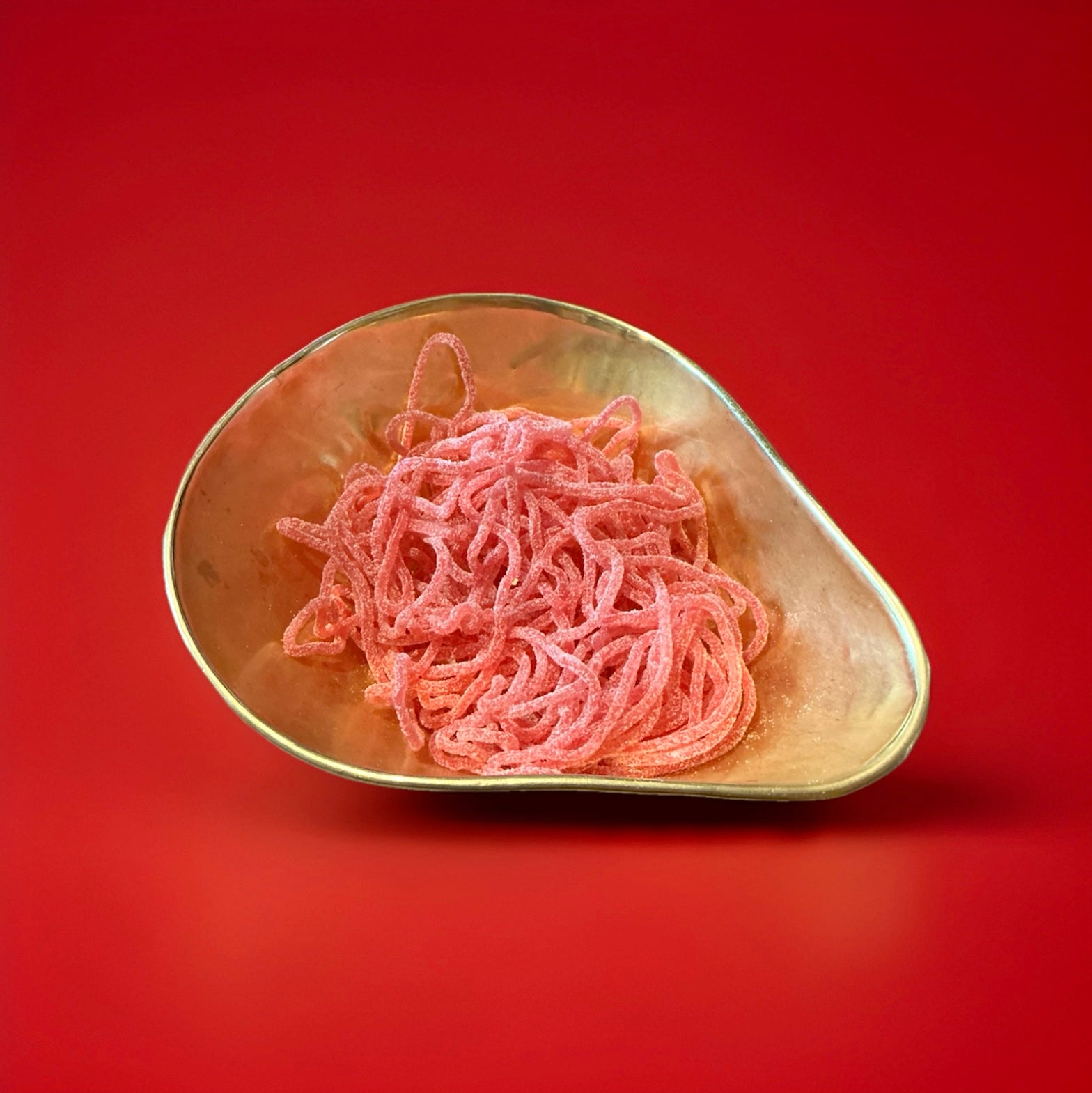 Red sour strawberry laces in a gold bowl with a red background 