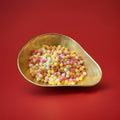 Hard boiled sherbet flavoured pips in a gold bowl on a red background 