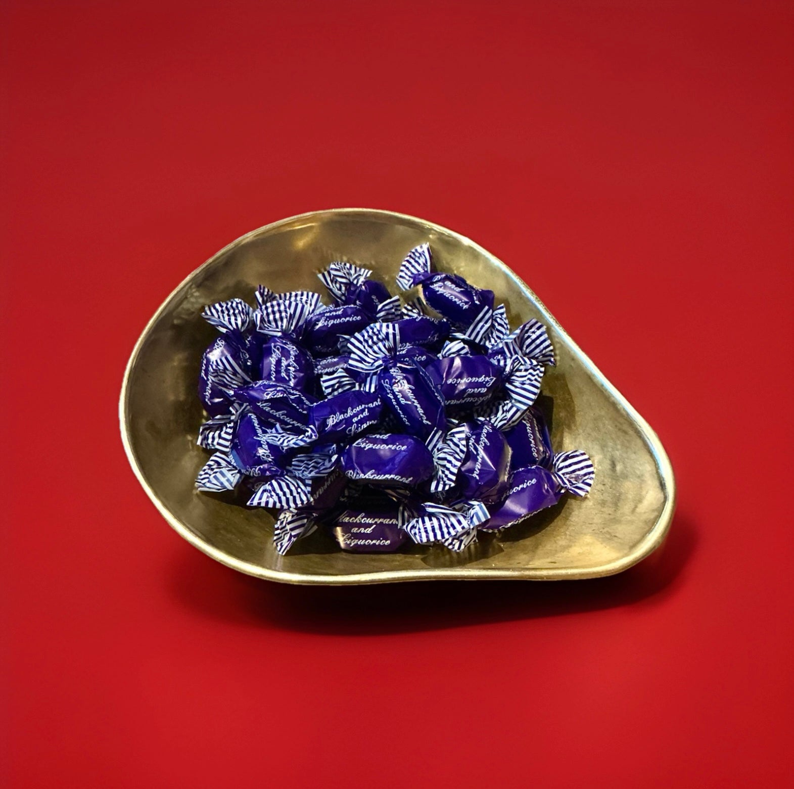 Individually wrapped hard boiled blackcurrant flavoured sweets with a chewy liquorice toffee centre in a purple wrapper in a gold bowl on a red background 